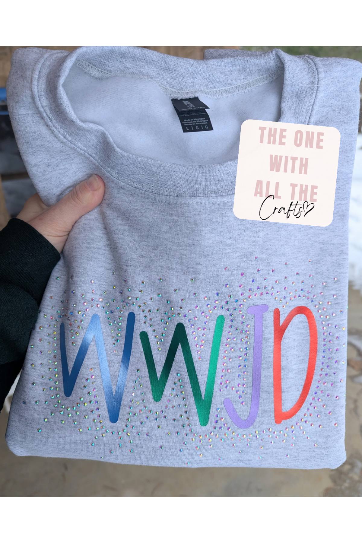 Gray sweatshirt with colorful 'WWJD' text and a tag on a neutral background