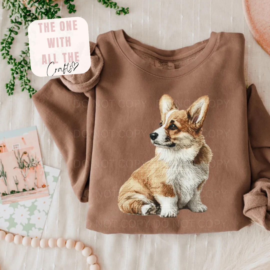 Brown sweatshirt with a corgi graphic on a light wooden surface.
