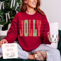 A woman wearing a festive red sweatshirt with the word 'JOLLY' in red and green polka-dot patterned letters, sitting on a couch and holding a mug.