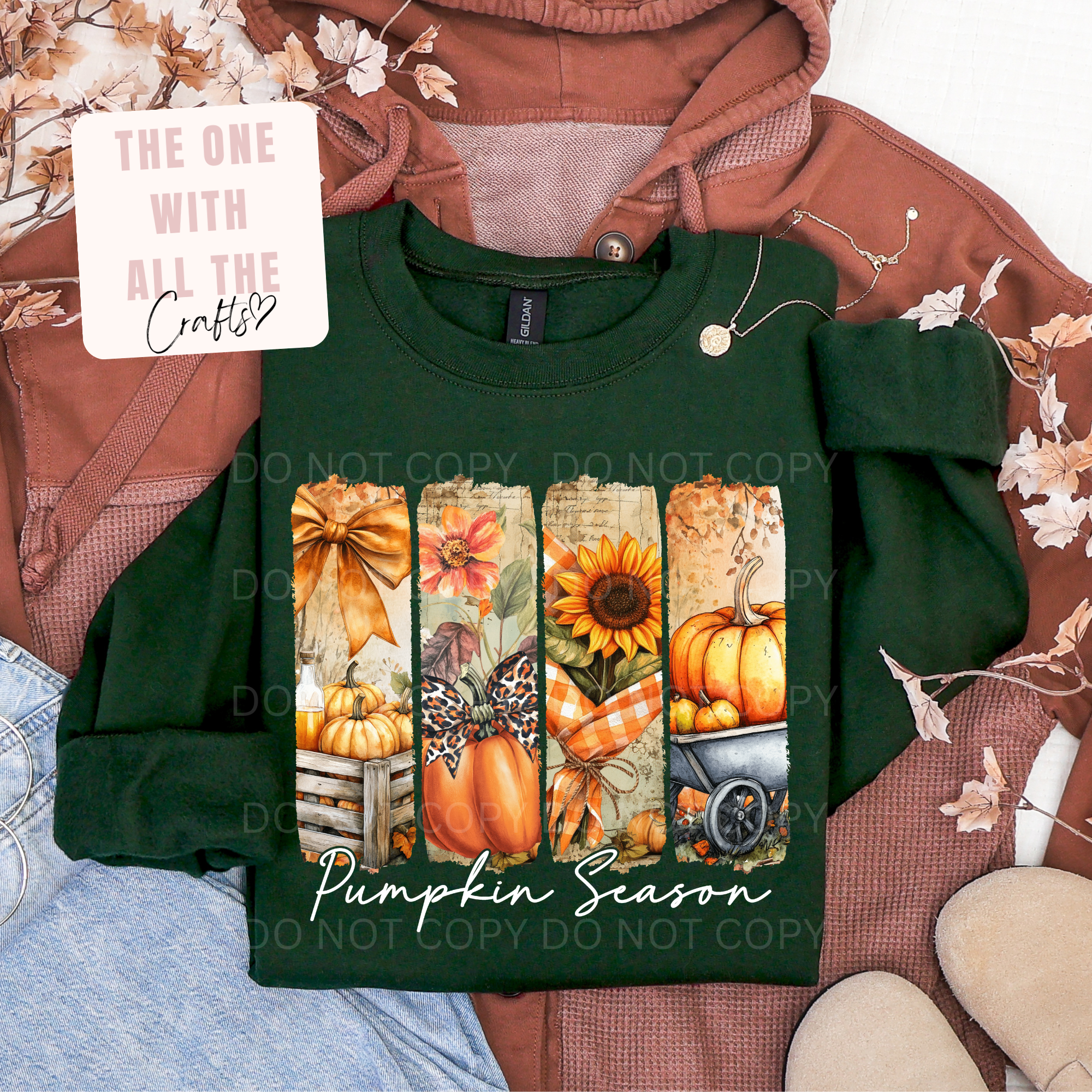 A dark green long-sleeve t-shirt featuring a vertical autumn-themed graphic print with pumpkins, sunflowers, and fall foliage, styled in a flat-lay arrangement with a brown hoodie, jeans, and a decorative card.