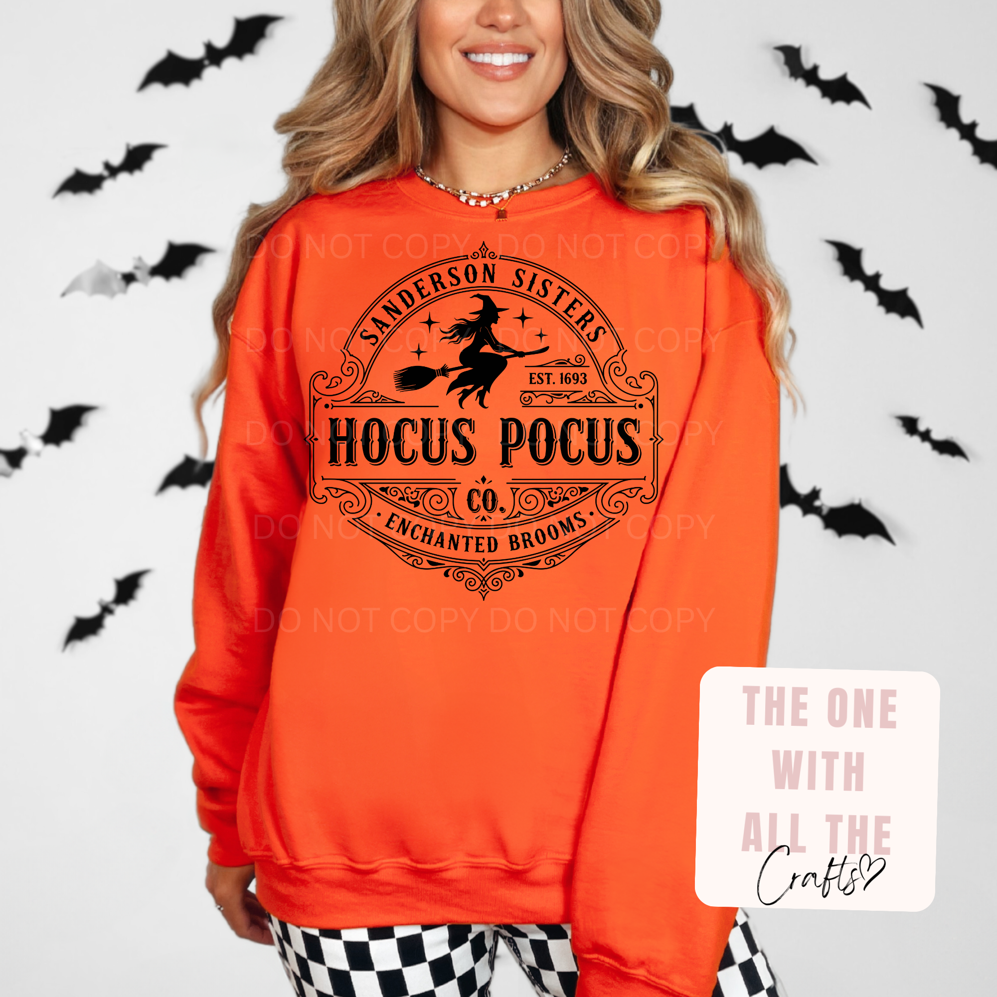 A woman wearing a bright orange crewneck sweatshirt with a black 'Hocus Pocus' graphic on the front. The graphic features a witch riding a broomstick with the text 'Sanderson Sisters Hocus Pocus Co Enchanted Brooms'.